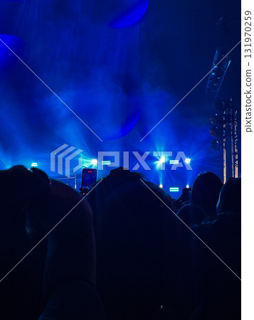 A rock concert with black silhouettes of fans enjoying the musical performance.Blue lights on a blurred stage in the background A rock concert with black silhouettes of fans enjoying the musical performance.Blue lights on a blurred stage in the background 131970259