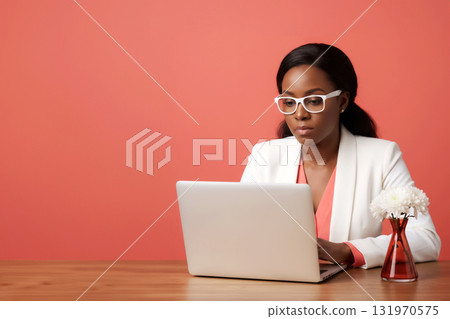 african american woman in a white jacket and glasses works on a laptop against a coral wall 131970575