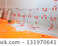 Workers are installing marble tiles on kitchen wall with tools spacers scattered on orange floor. 131970641