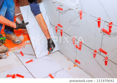 Expert tiler laying large marble tiles on bathroom wall using spacers to ensure even gaps. 131970642