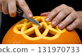 Hands carving a Halloween pumpkin with a geometric design 131970733