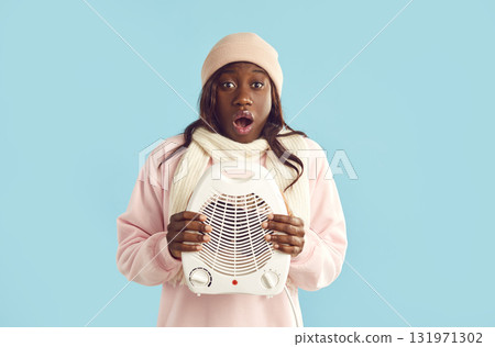 African American woman freezes in cold winter and tries to warm up with electric fan heater 131971302