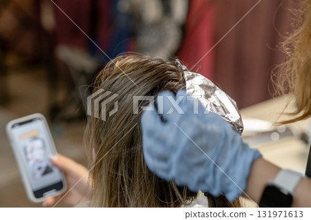A stylist applies hair color while the client checks their phone, showcasing a trendy and vibrant hair transformation session. A stylist applies hair color while the client checks their phone, showcasing a trendy and vibrant hair transformation session. 131971613