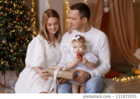 Happy young family with baby girl celebrating Christmas at home near decorated tree Happy young family with baby girl celebrating Christmas at home near decorated tree 131972055