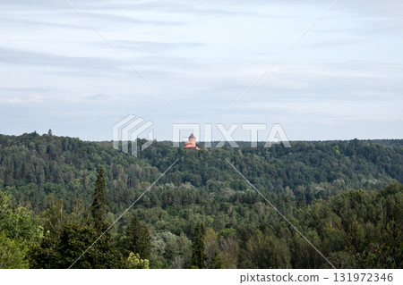 Scenic landscape with medieval red brick castle on hill surrounded by dense green forest under Scenic landscape with medieval red brick castle on hill surrounded by dense green forest under 131972346