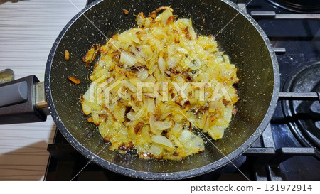 Chopped onions frying in a pan on the stovetop during evening meal preparation at a cozy home kitchen 131972914