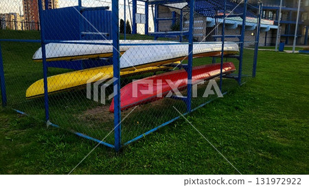 Colorful kayaks stored securely in a fenced area at a waterfront park during the evening Colorful kayaks stored securely in a fenced area at a waterfront park during the evening 131972922