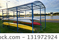Boats stored under shelter near a calm water body during a sunny afternoon in a recreational area 131972924
