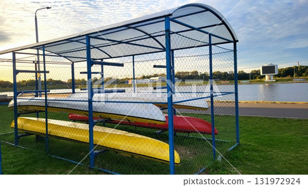 Boats stored under shelter near a calm water body during a sunny afternoon in a recreational area Boats stored under shelter near a calm water body during a sunny afternoon in a recreational area 131972924