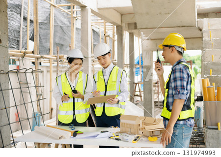 Engineers and architects collaborating on-site with safety gear, blueprints, and tools, showcasing teamwork, 131974993