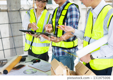Engineers and architects collaborating on-site with safety gear, blueprints, and tools, showcasing teamwork, 131975006