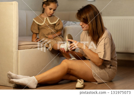 Mother helps daughter put on shoes at home Mother helps daughter put on shoes at home 131975073