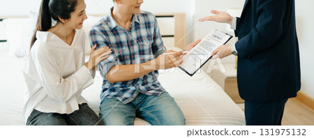 Asian man Real estate broker agent showing a house detail in her file to the young Asian couple lover looking and interest to buy it. Asian man Real estate broker agent showing a house detail in her file to the young Asian couple lover looking and interest to buy it. 131975132