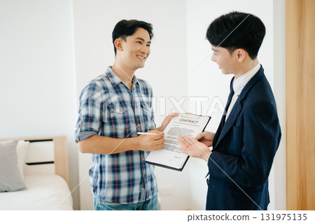 Asian man Real estate broker agent showing a house detail in her file to the young Asian couple lover looking and interest to buy it. 131975135