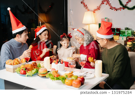 Celebrate Christmas with family in a cozy, festive setting. Santa hats, gifts, and delicious food capture the warmth, joy 131975284