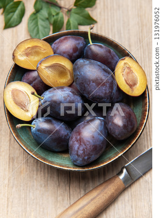 Fresh ripe plums in bowl on wood surface 131976052