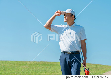 一名男子手持推桿和高爾夫球桿在高爾夫球場上行走 一名男子手持推桿和高爾夫球桿在高爾夫球場上行走 131976347