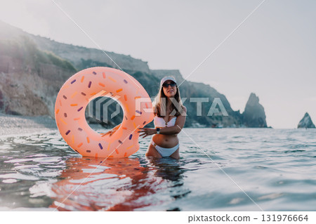 Woman, ocean, donut float, young woman stands in sea holding inflatable donut enjoying summer vacation at rocky coast. 131976664