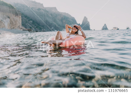 Woman ocean vacation, young woman relaxing on a pink inflatable ring in the calm ocean near cliffs. Woman ocean vacation, young woman relaxing on a pink inflatable ring in the calm ocean near cliffs. 131976665