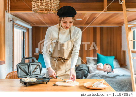 一位繫著圍裙的亞洲年輕女子正在用熱三明治機製作熱三明治 131978854