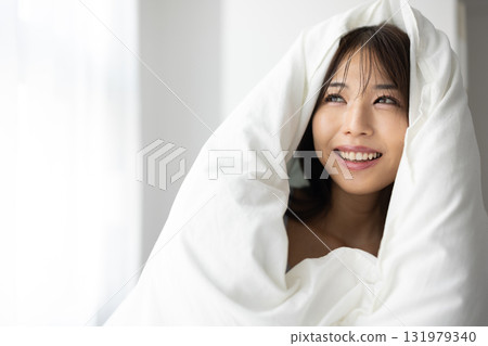 一位微笑的年輕女子裹著被褥，沐浴在清晨的陽光下 131979340