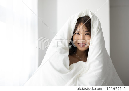 一位微笑的年輕女子裹著被褥，沐浴在清晨的陽光下 131979341