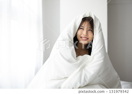 一位微笑的年輕女子裹著被褥，沐浴在清晨的陽光下 131979342