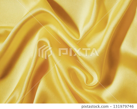 A close-up, full-frame background of silky, golden-yellow satin fabric. The material is artfully draped and folded, creating a dynamic play of light and shadow across its smooth, reflective surface A close-up, full-frame background of silky, golden-yellow satin fabric. The material is artfully draped and folded, creating a dynamic play of light and shadow across its smooth, reflective surface 131979746