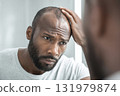 Worried man examining thinning hair in mirror 131979874