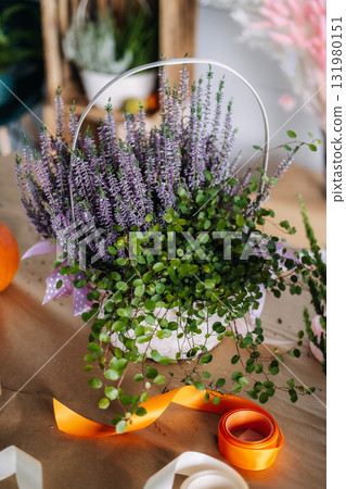 Basket arrangement with purple heather and trailing greenery set beside a pumpkin and ribbons on a florist table. Local florist Thanksgiving visual, natural branding content Basket arrangement with purple heather and trailing greenery set beside a pumpkin and ribbons on a florist table. Local florist Thanksgiving visual, natural branding content 131980151
