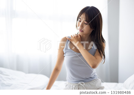 A young woman massaging her shoulders while basking in the morning sun through the window 131980486