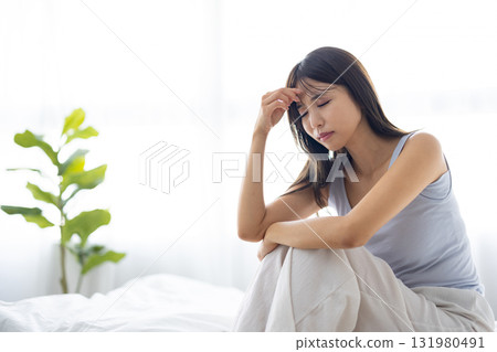 A young woman with an unpleasant expression as she bathes in the morning sun through the window 131980491