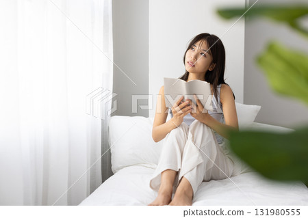 A young woman reading a book in bed while basking in the morning sun through the window A young woman reading a book in bed while basking in the morning sun through the window 131980555