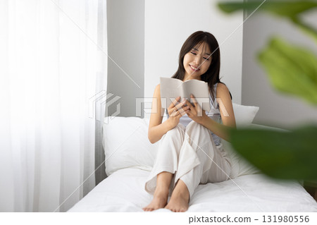 A young woman reading a book in bed while basking in the morning sun through the window A young woman reading a book in bed while basking in the morning sun through the window 131980556