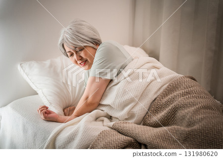 A gray-haired senior woman with a painful expression after waking up in her bedroom A gray-haired senior woman with a painful expression after waking up in her bedroom 131980620