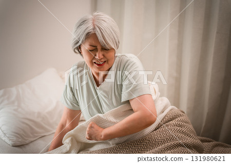 A gray-haired senior woman with a painful expression after waking up in her bedroom 131980621