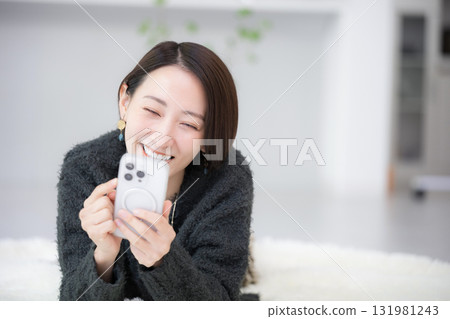 Close-up of a cute woman lying face down in a room and tapping on her smartphone 131981243
