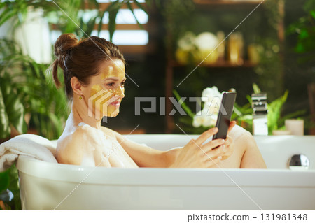 Bathtub Bliss: Woman with Mask and Smartphone Bathtub Bliss: Woman with Mask and Smartphone 131981348