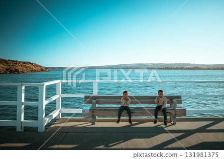 Two Children Are Relaxing and Enjoying Time by the Serene Waterfront Two Children Are Relaxing and Enjoying Time by the Serene Waterfront 131981375