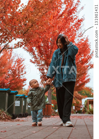 Autumn Stroll: Mother and Child Walking Amidst Colorful Fall Leaves 131981431