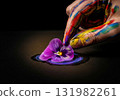 Artist's hand covered in paint gently placing a purple pansy flower on a wet paint stroke 131982261