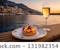 Fruit tartlet and a glass of champagne on a table with a beautiful coastal city at sunset 131982354