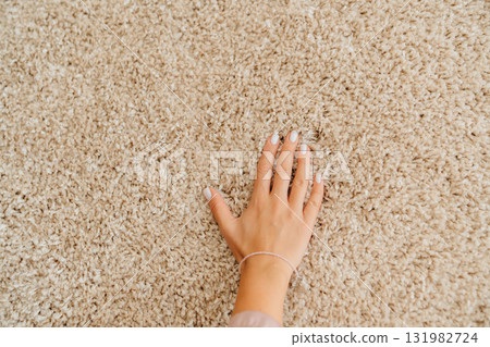 a woman's hand touching the beige Interior pile carpet made of polypropylene. a woman's hand touching the beige Interior pile carpet made of polypropylene. 131982724