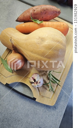 Fresh vegetables arranged on a wooden cutting board including butternut squash, sweet potato, carrot, onion, and garlic. Concept of healthy cooking ingredients and autumn seasonal food Fresh vegetables arranged on a wooden cutting board including butternut squash, sweet potato, carrot, onion, and garlic. Concept of healthy cooking ingredients and autumn seasonal food 131982929