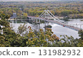 Suspension pedestrian bridge crossing a calm river surrounded by autumn trees. Concept of urban landscape, travel destination, and architectural connection with nature 131982932