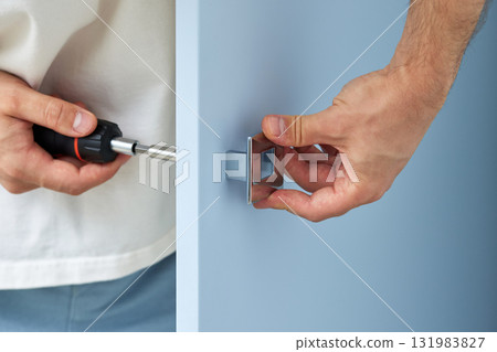 worker installing handle of blue cabinet door with screwdriver, close-up. furniture assembly service worker installing handle of blue cabinet door with screwdriver, close-up. furniture assembly service 131983827