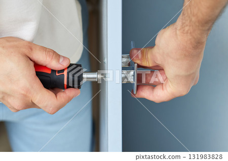 worker installing new handle of cabinet door with screwdriver, close-up. furniture assembly service 131983828