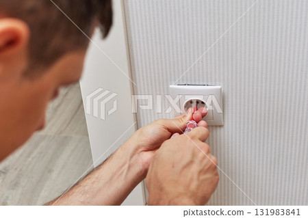 electrician installing electrical socket in white plastic frame with a screwdriver at home electrician installing electrical socket in white plastic frame with a screwdriver at home 131983841