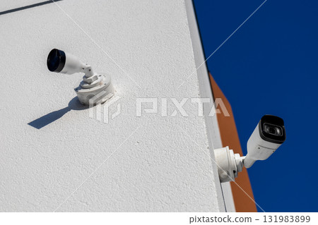 Two CCTV cameras mounted on a building monitor the area for safety and security, ensuring protection against potential threats Two CCTV cameras mounted on a building monitor the area for safety and security, ensuring protection against potential threats 131983899
