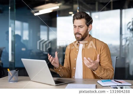 Man leading a virtual business meeting from a professional office, engaging in a video call on a laptop, gesturing and explaining ideas during a remote work conference 131984288